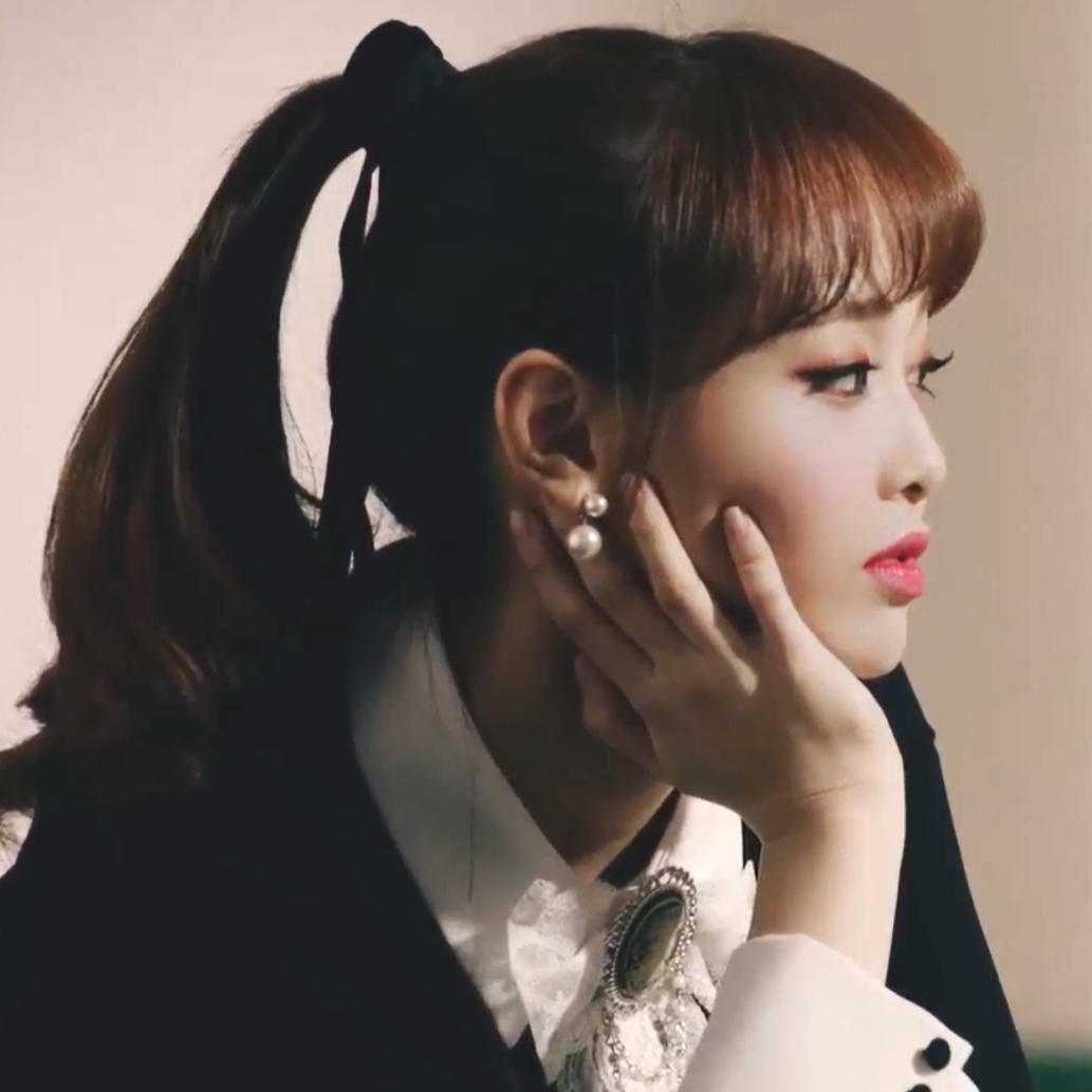 Chuu from the 'Heart Attack' music video. She has long reddish-brown hair tied into a ponytail and is wearing a black dress. She is resting her head on her hand.